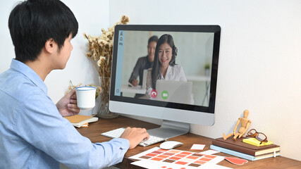 Obraz premium Cropped image man is making a video call with his colleague while sitting in front of a computer monitor at the wooden working desk.
