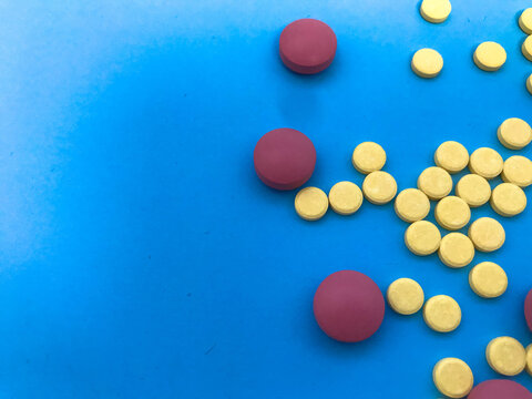 colored pink, yellow pills volumetric and round in shape on a blue matte and paper background. health medications. herbal medicines. medical background