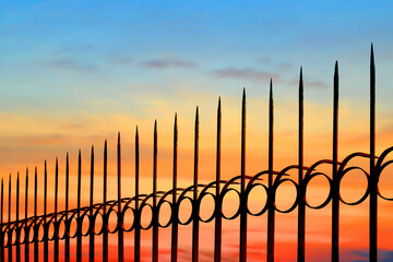Silhouette arrow spiky metal fence against beautiful sunset sky background, side view with copy space