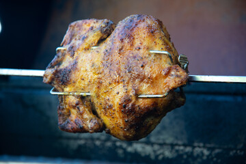 Juicy chicken rotating on a rotisserie on a grill