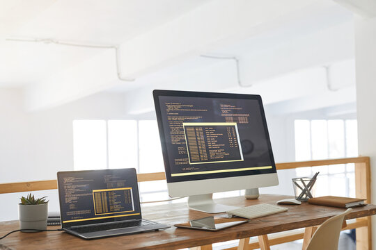 Background image of two computers with programming code on screen in minimal home office interior with wooden accents, copy space