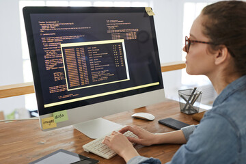 Portrait of young woman writing programming code on computer screen while working at desk in...