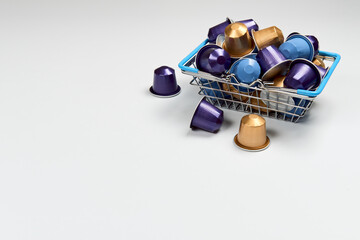 Caffeine, hot drinks and objects concept - close up blue, purple and golden capsules or pods for coffee mashine in shopping basket on white isolated background. Top view with space for text. 