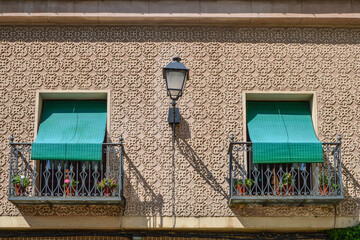 facade decorated with geometric reliefs and two balconies with green awnings and a lamppost in the middle in Segovia. Spain.