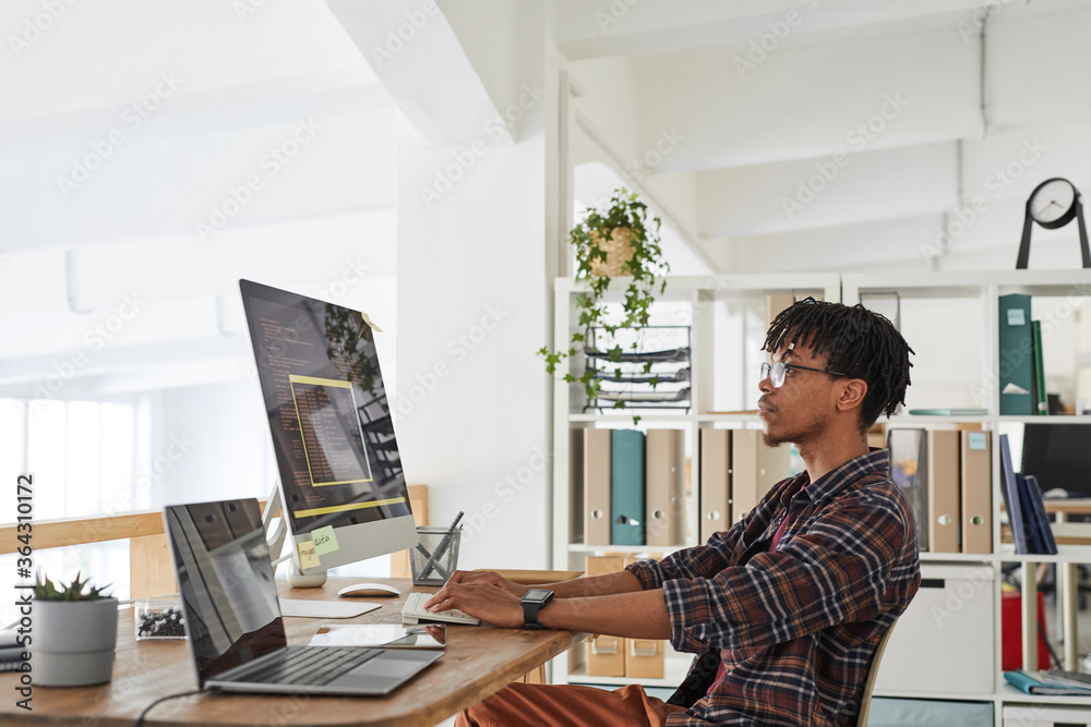 Wall mural side view portrait of african-american it developer typing on keyboard with black and orange program