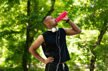 Thirsty young athlete drinking water from bottle after his training at park