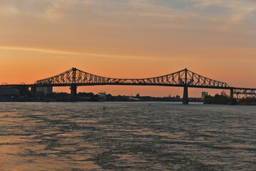 A skyline view a steel bridge across a river at sunset. Jacques Cartier Bridge across Saint Laurent river, Montreal, Quebec, Canada