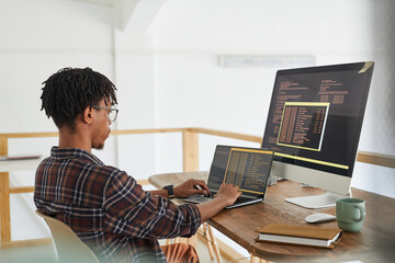 African-American IT developer typing on keyboard with black and orange programming code on computer...