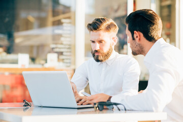 Two professional businessmen using computer sitting outdoors - Businessmen colleague having meeting outdoors - remote working, business, technology concept