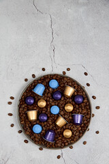 Caffeine, hot drinks and objects concept - close up colorful capsules or pods for coffee mashine with some roasted grains in plate on gray concrete background. Top view with space for text. 