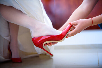 Bridesmaids helping bride to put her red wedding shoes on. Preparation moments and details.
