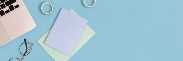 Banner with laptop, glasses and stationery on a blue pastel background. Office concept with copy space.