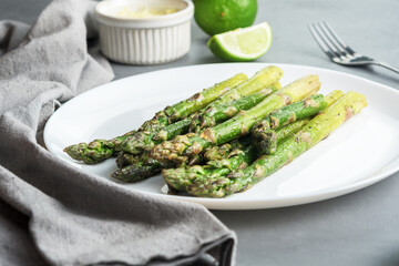 Appetizingly cooked asparagus with pieces of lime on a grey concrete table.