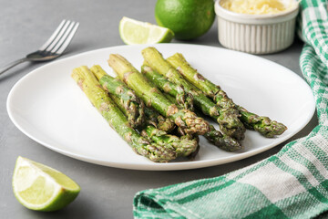 Appetizingly cooked asparagus with pieces of lime on a grey concrete table.