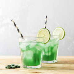 Two glasses of refreshing lemonade with chlorella and lime on a wooden table.