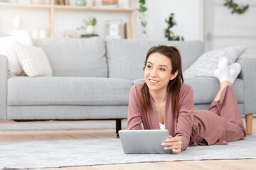 Pensive young woman using digital tablet at home, relaxing on floor