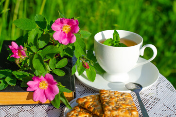 A Cup of green tea with a mint leaf, flowers, and a book on a table in the garden. Evening tea with cookies. Summer village concept. Vintage banner.