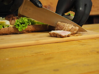the chef slices and puts the meat on a mega sandwich with salad leaves.
