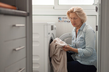 An aged woman is trying to wash in a new washing machine. facilitating domestic work.