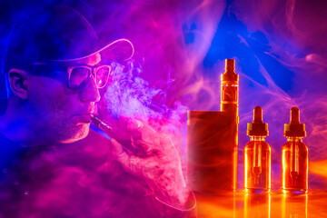 E-cigarette smoker. The concept of vaping in a smoky neon background. A man in glasses and a baseball cap smokes a VAPE. Smoker and Smoking accessories on a dark background in smoke.