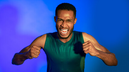 Emotional Black Sportsman Shouting Clenching Fists Over Blue Background, Panorama