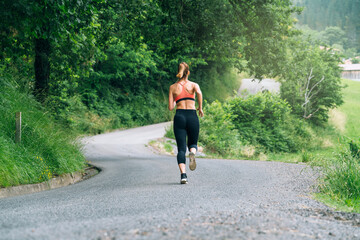 rear view of a girl running across a road through a forest