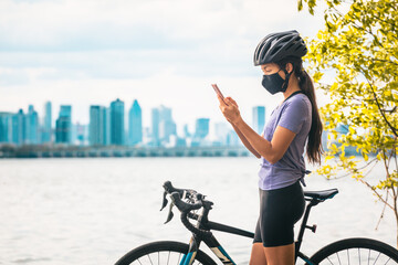 Biking cyclist using mobile phone for contact tracing app wearing COVID-19 face mask as coronavirus...