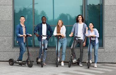 Five friends standing with motorized kick scooters