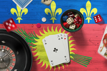 Guadeloupe casino theme. Aces in poker game, cards and chips on red table with national flag background. Gambling and betting.