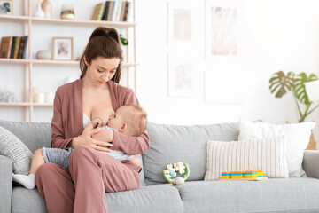 Breastfeeding Concept. Young woman lactating her toddler baby on couch at home