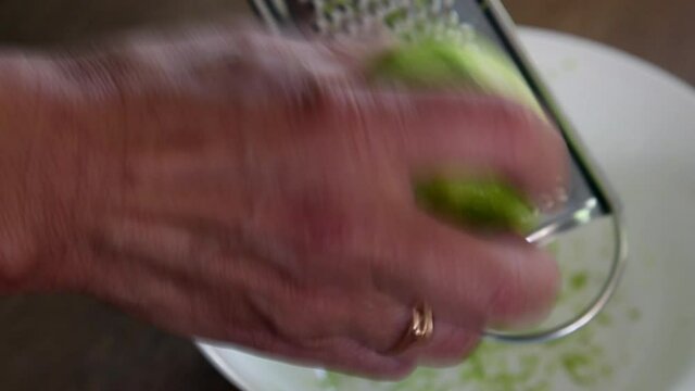 Hand of woman zesting lime fruit with grater, close-up footage