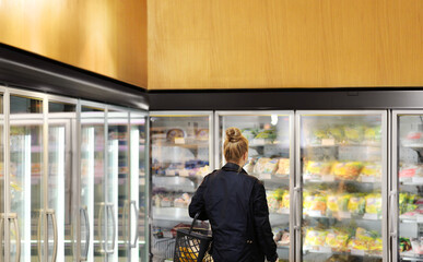 Woman choosing frozen food from a supermarket freezer. purchasing a packet of meat at the supermarket