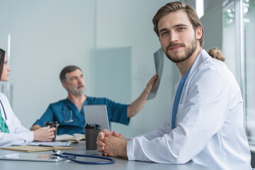 Portrait of young man doctor in white coat sitting in a meeting with business people negotiating medical insurance.