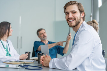 Obraz premium Portrait of young man doctor in white coat sitting in a meeting with business people negotiating medical insurance.