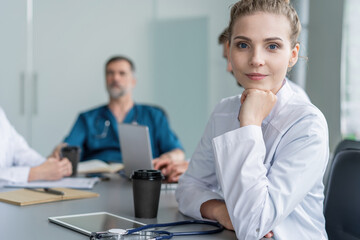 Obraz premium Young female doctor sitting and looking at camera during the meeting in hospital