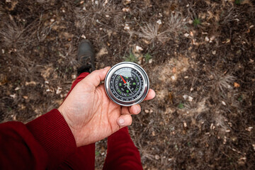 Compass in hand on a background of legs, Close-up. The concept of travel, hiking, vacation. Copy space.
