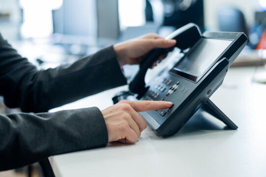 Closeup Female Hand On Landline Phone In Office. Faceless Woman In A Suit Works As A Receptionist Answering The Phone To Customer Calls.