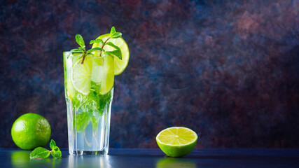 Mojito cocktail with lime and mint in tall glass. Fresh mojito in glass on a dark background....