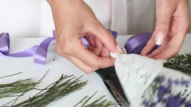 A woman is wrapping lavender flowers in craft paper. On the table are lavender flowers