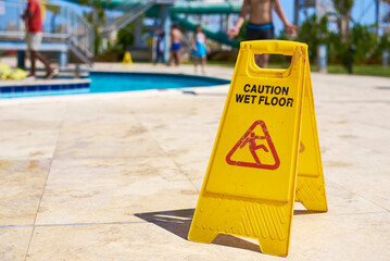 Yellow wet floor caution sign in summer day, closeup