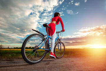 Sports training on a bicycle. Beautiful girl in a sports suit on a sunset background. The concept...