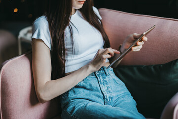 Beautiful young caucasian woman sitting on a pink sofa and using tablet computer. Work at home.