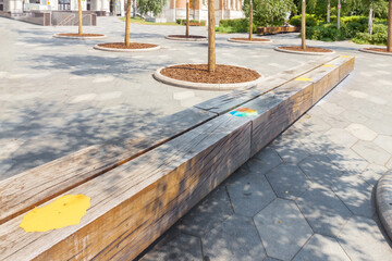 Social distancing rules marked yellow sticker marking on wooden bench alternate seating in local public city park, to reduce risk of further transmission, safety measures