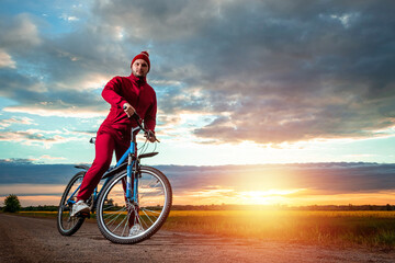 Fototapeta na wymiar Sports training on a bicycle. A man in a tracksuit on a sunset background. The concept of a healthy lifestyle, cardio training, physical activity. Copy space.