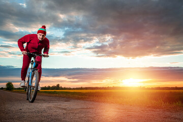 Fototapeta premium Sports training on a bicycle. A man in a tracksuit on a sunset background. The concept of a healthy lifestyle, cardio training, physical activity. Copy space.