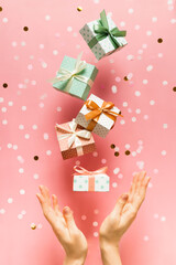 Polka dot pattern gift box with ribbon falling and female hands on pink background, levitation