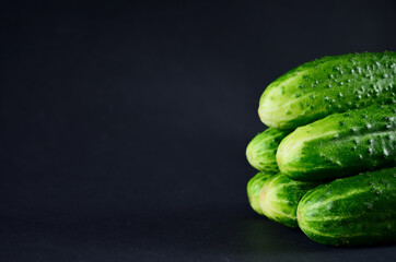 Fresh green cucumbers lie on top of each other on a black background of vegetables for a healthy diet with copy space