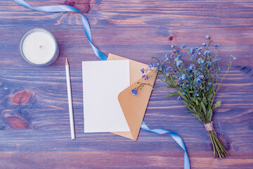 Mockup white wedding invitation and envelope with blue flowers on a wooden background