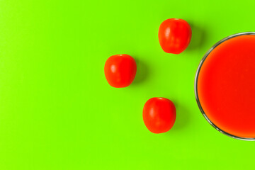 red tomato and a glass of tomato juice on a green background. hard shadow. isolate