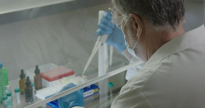 A lab technician working with pathogen behind protective laboratory ventilation hood.